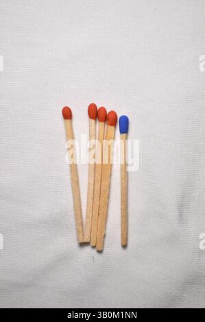 Une seule allumette bleue se distingue parmi quatre rouges, disposées soigneusement sur un fond blanc Uni. Banque D'Images