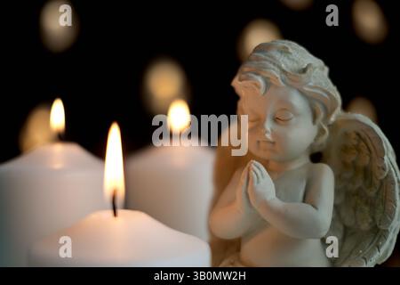 Statue d'ange en porcelaine dans la pose de prière avec les mains pliées, éclairée par des bougies brillantes, symbolisme spirituel et religieux Banque D'Images