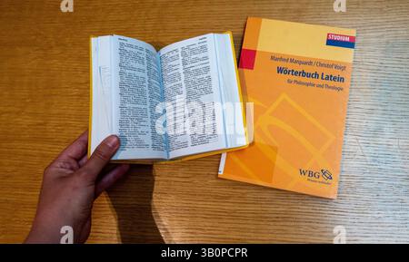 Munich, Allemagne. 24 avril 2025. Un ancien dictionnaire grec-allemand ouvert d'une main et un dictionnaire latin-allemand fermé reposent sur une table. L'éducation humaniste joue encore un rôle majeur dans les lycées bavarois. Selon le ministère de la culture, la matière latine était offerte à 98% des lycées de l'État au cours de l'année scolaire 2023/2024 et le grec ancien à 12%. Crédit : Leonie Asendorpf/dpa/Alamy Live News Banque D'Images