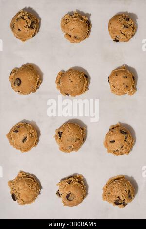 Rangées de boules de pâte à biscuits aux pépites de chocolat disposées sur du papier parchemin blanc, prêtes à être cuites. Banque D'Images