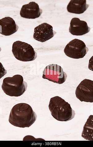 L'image montre des bonbons au chocolat noir assortis sur marbre, avec diverses formes et textures. Un chocolat est ouvert. Banque D'Images