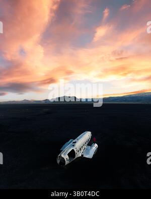 L'avion DC-3 a fait naufrage sur la plage de sable noir islandaise de Solheimasandur sous un ciel de coucher de soleil vif et coloré avec une personne en rouge ajoutant échelle et contraste. Banque D'Images