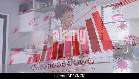 Image de cellules virales et graphiques sur une femme biraciale travaillant à domicile Banque D'Images