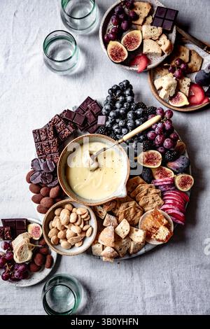 Une élégante planche de charcuterie avec une variété de fromages, figues, raisins, amandes, chocolat, pain et craquelins, avec une casserole de fromage crémeux trempette sur Banque D'Images