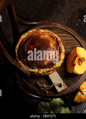 Cheesecake basque à la citrouille sur une chaise vintage sombre, esthétique automnale rustique et sombre Banque D'Images