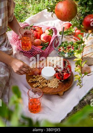 scène de pique-nique vue sur la vie avec grenades fraîches, noix, pignons de pin et fromage blanc crémeux exposés sur une planche de bois, pomegra naturel ensoleillé Banque D'Images