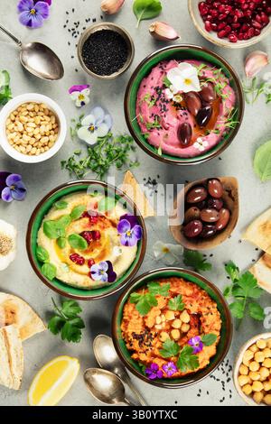 Un trio de houmous coloré aux saveurs classiques, de betterave et de poivron rouge rôti, garni d'herbes fraîches, d'olives et de fleurs comestibles. Parfait pour foo Banque D'Images