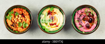 Un trio vibrant de houmous en différentes saveurs, classique, betterave et poivron rouge rôti, garni d'herbes fraîches et de garnitures, parfait pour les menus, Banque D'Images