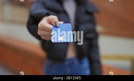 Femme tenant une carte de crédit dans une rue urbaine avec un fond flou, mettant en valeur la technologie de paiement dans un cadre urbain extérieur. Banque D'Images