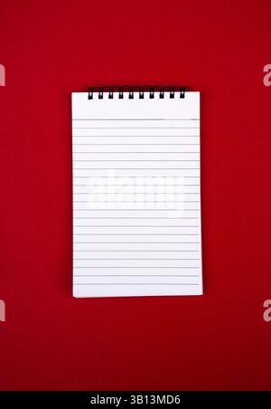 Une pose à plat simple et visuellement frappante d'un cahier vierge placé sur un fond rouge. Utile pour l'écriture éducative, motivante ou professionnelle Banque D'Images