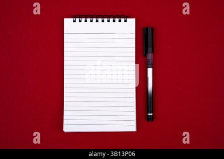 Image haute résolution d'un cahier ouvert vierge avec un stylo, isolé sur un fond rouge vif. Idéal pour mettre en valeur la créativité, la prise de notes, productivi Banque D'Images