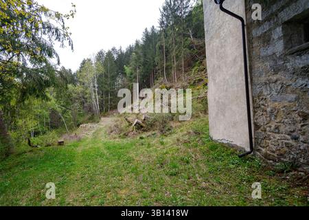 Bad Illstern, italie., lieu perdu. Plan extérieur d'un coin d'un bâtiment, mur de pierre et de plâtre, avec un paysage forestier au-delà. L'herbe et un chemin le sont Banque D'Images