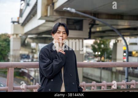 Un Japonais dans la vingtaine portant une veste noire se trouve à Minato Mirai, Yokohama, préfecture de Kanagawa. Il est assis sur un banc, regardant au loin, Banque D'Images