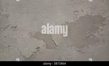Gros plan d'un mur de béton rugueux et usé avec une texture granuleuse, présentant des fissures et des crevasses. La couleur est un gris terne, sourd avec subtilité Banque D'Images