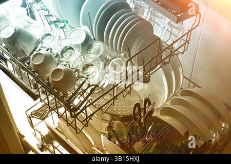 Détail d'un lave-vaisselle ouvert avec plateaux retirés rempli de vaisselle fraîchement lavée éclairée par une lumière froide et chaude rétroéclairée. Vue surélevée. Banque D'Images