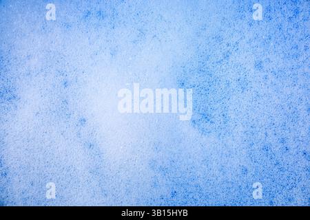 Fond avec texture de mousse du produit de nettoyage ou de bain sur la surface de l'eau de couleur bleue. Vue de dessus. Banque D'Images