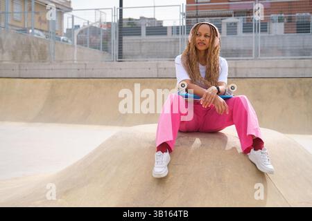 Patineur élégant écoutant de la musique dans le skate Park assis sur la rampe Banque D'Images