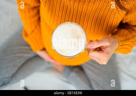 Une vue rapprochée montre une mère qui tient du latte tout en méditant sur la nutrition pendant la grossesse. Scène confortable de choix de style de vie équilibrés. Banque D'Images
