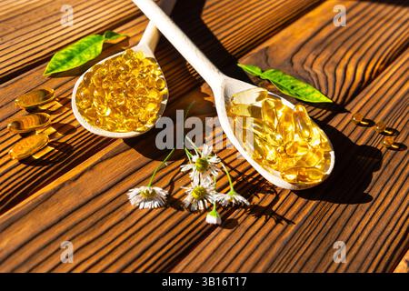 Cuillères en bois avec capsules d'huile de poisson sur table rustique. Deux cuillères en bois remplies de capsules d'huile de poisson dorées reposent sur une table en bois rustique. Banque D'Images