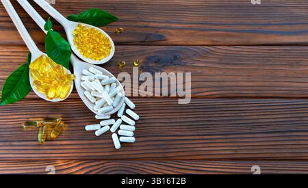 Capsules assorties et vitamines dans des cuillères en bois avec des feuilles vertes. Cette image présente une variété de compléments alimentaires et de vitamines disposés dans Banque D'Images