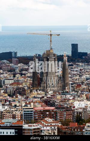 Vue aérienne de Barcelone avec l'emblématique basilique de la Sagrada Familia en construction, entourée de bâtiments urbains et de la mer Méditerranée Banque D'Images