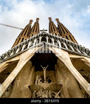 Une vue en angle bas de la Sagrada Familia à Barcelone, mettant en valeur ses détails architecturaux complexes et ses flèches imposantes dans un ciel nuageux. Banque D'Images