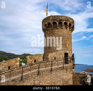 Une tour de pierre historique avec une structure ronde, avec un drapeau sur le dessus. La tour fait partie d'un château surplombant la mer, entouré de verdure et Banque D'Images