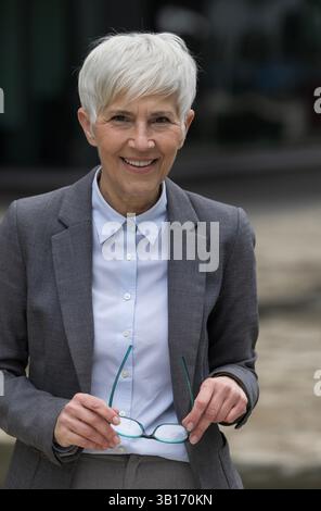 Femme d'affaires âgée souriant à la caméra et enlevant ses lunettes devant le bâtiment Banque D'Images