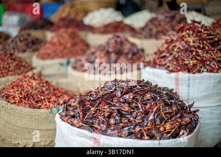 Piments chili à vendre Marché Zegyo Mandalay Myanmar | MANDALAY, Myanmar — Des sacs de piments chili séchés de qualités variées remplissent un étal de produits dans le marché de rue autour du marché Zegyo, le centre commercial historique du centre de Mandalay. Les piments chili font partie des produits les plus vendus ici, répondant à la demande à la fois des acheteurs domestiques et des commerçants redistribuant les stocks dans la Haute-Birmanie. Zegyo fonctionne comme le principal marché de gros et de détail de Mandalay depuis que le roi Mindon a établi la ville dans les années 1850, en faisant un conduit de longue date pour les produits agricoles et les épices de toute la région. Banque D'Images