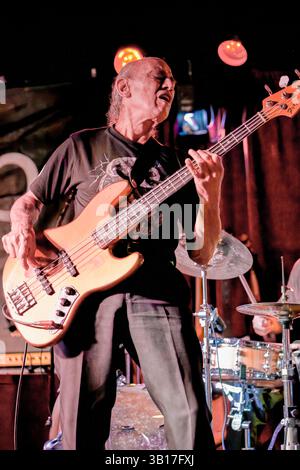 Norman Watt-Roy joue de sa guitare basse électrique avec intensité sur une scène faiblement éclairée, éclairée par des projecteurs chauds au Half Moon, Putney. Banque D'Images