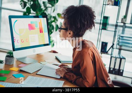 Jeune femme professionnelle examinant les données sur un ordinateur dans un espace de travail moderne au cours d'une journée de travail productive Banque D'Images