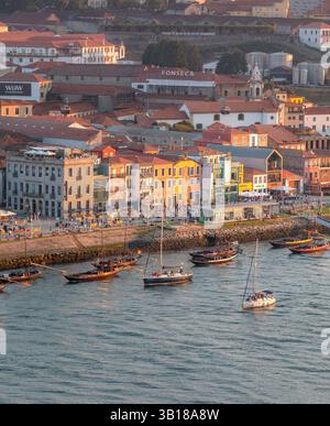 Vue panoramique des bâtiments historiques colorés le long de Cais de Gaia, Porto, Portugal, avec des bateaux traditionnels Rabelo amarrés sur le fleuve Douro. Banque D'Images