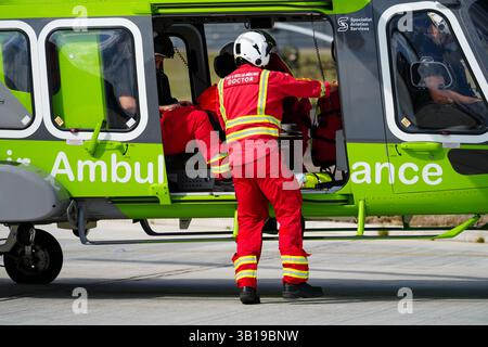 Un médecin ambulancier de l'air sort d'un hélicoptère vert, se préparant à une intervention médicale d'urgence. Banque D'Images