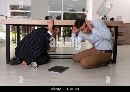 Les employés ont peur de se cacher sous le bureau pendant le tremblement de terre Banque D'Images