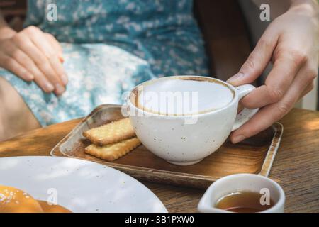 Un moment de détente est capturé alors qu'une personne profite d'une tasse de café fraîchement infusé recouvert de mousse de lait. Le cadre est un café en plein air avec l naturel Banque D'Images