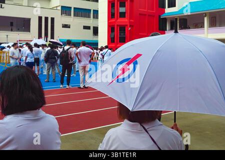 Singapour 2025 avr23 - jour de la nomination aux élections générales. Un partisan du PAP avec parapluie regarde les gens se rassembler à l'école de Chongfu, attendant le Ret Banque D'Images