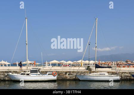 Molo Eugenio Guidotti quai avec voiliers amarrés, parasols et les Alpes Apuanes en arrière-plan en été, Viareggio (Lucques), Toscane, Italie Banque D'Images