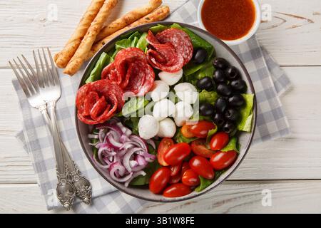 Salade de pizza italienne fraîche avec saucisses, mozzarella, tomates, olives, oignons, sauce à la laitue romaine et à la vinaigrette servie avec des gressins Banque D'Images