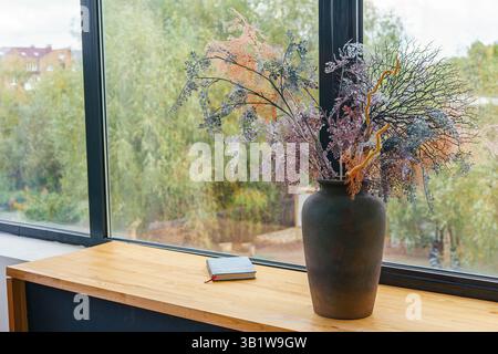 Bouquet de fleurs séchées artificielles et décoratives dans un pot en argile brune sur le rebord de la fenêtre dans le salon, appartement. Décoration de la maison, détail de l'intérieur design Banque D'Images
