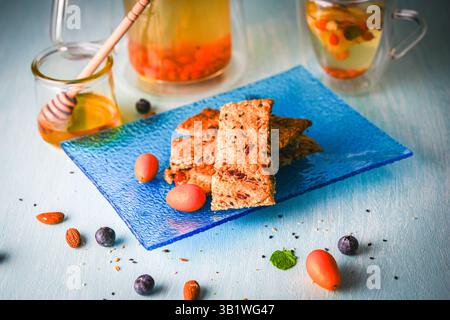 Craquelins avec des graines de lin, des noix et des graines de sésame sur une assiette bleue et du thé avec du citron et du miel sur la table sur un fond gris. Photo de haute qualité Banque D'Images