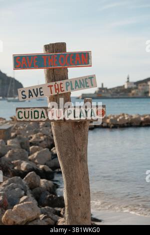 Holzschild mit Umweltschutz-Botschaften 'Save the Ocean', 'Save the Planet' und 'Cuida la Playa' an einer felsigen Küste mit Meerblick und einer klein. Banque D'Images