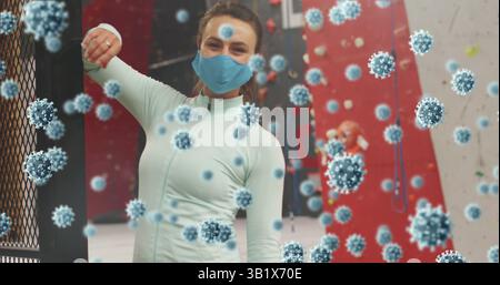 Bras levant femme dans le masque supérieur sarcelle à la salle de gym d'escalade, avec des murs rouges et des graphiques de virus Banque D'Images