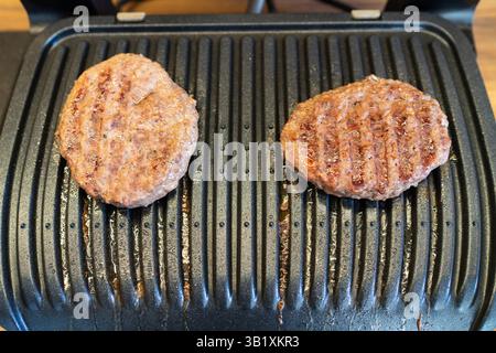Gros plan de la cuisson de viandes juteuses pour hamburgers faits maison sur la surface d'un gril à contact électrique. Banque D'Images