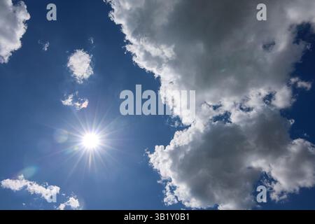 La lumière du soleil se répand à travers un mélange de nuages blancs et gris dans un ciel bleu éclatant, créant une superbe toile de fond pour une journée d'été parfaite Banque D'Images