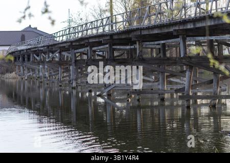 Un charmant pont piétonnier en bois s'étend sur la rivière, ses planches altérées offrant un chemin rustique à travers la nature. Le flux serein du ri Banque D'Images