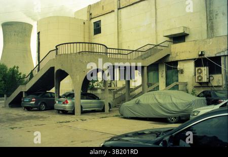 Bâtiment industriel avec tour de refroidissement et véhicules au premier plan 'ancien complexe industriel avec escalier en béton et tour de refroidissement Banque D'Images