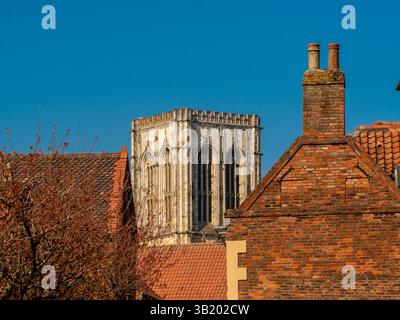 Tour centrale de York Minster encadrée entre des maisons historiques sur St Andrewgate, vue par une journée ensoleillée avec un ciel bleu à York, Royaume-Uni. Banque D'Images