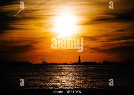 La silhouette de la Statue de la liberté à New York avec un ciel de coucher de soleil dramatique Banque D'Images