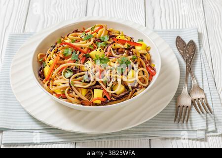 Salade de nouilles à la mangue thaïlandaise avec poivre, chou rouge, menthe et coriandre, vinaigrette à la sauce cacahuète dans un bol blanc sur une table en bois blanc Banque D'Images
