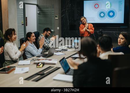 Les gens d'affaires multiculturels réfléchissent à des idées et applaudissent la présentation d'un membre de l'équipe tout en analysant les solutions du projet. Banque D'Images